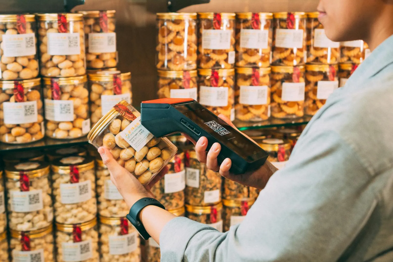 Individual scanning QR codes on jars in a store with a handheld device.