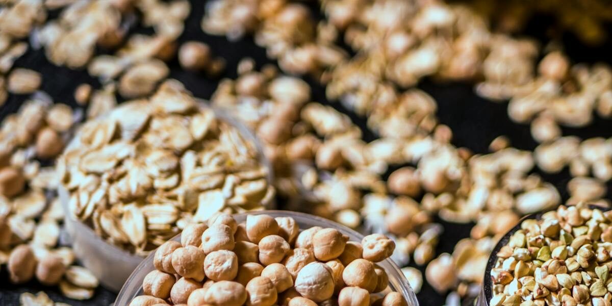 Close-up of assorted raw grains and seeds in cups on a dark background, showcasing variety and texture.