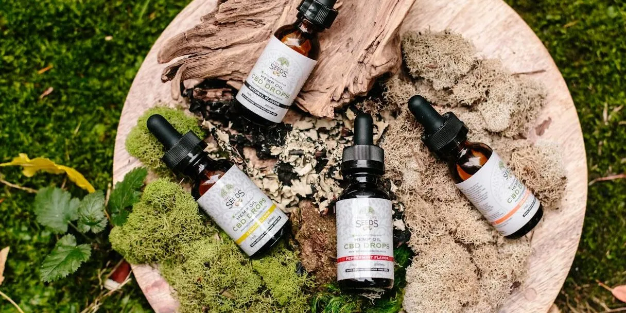 Natural CBD oil bottles with droppers on a wooden board surrounded by moss and leaves.