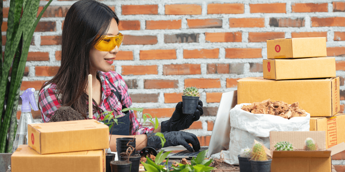 A woman wearing an apron and glasses tends to a potted plant, focused on her gardening task.