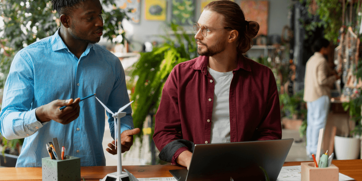 Two men engaged in conversation at a table, with a laptop open between them.