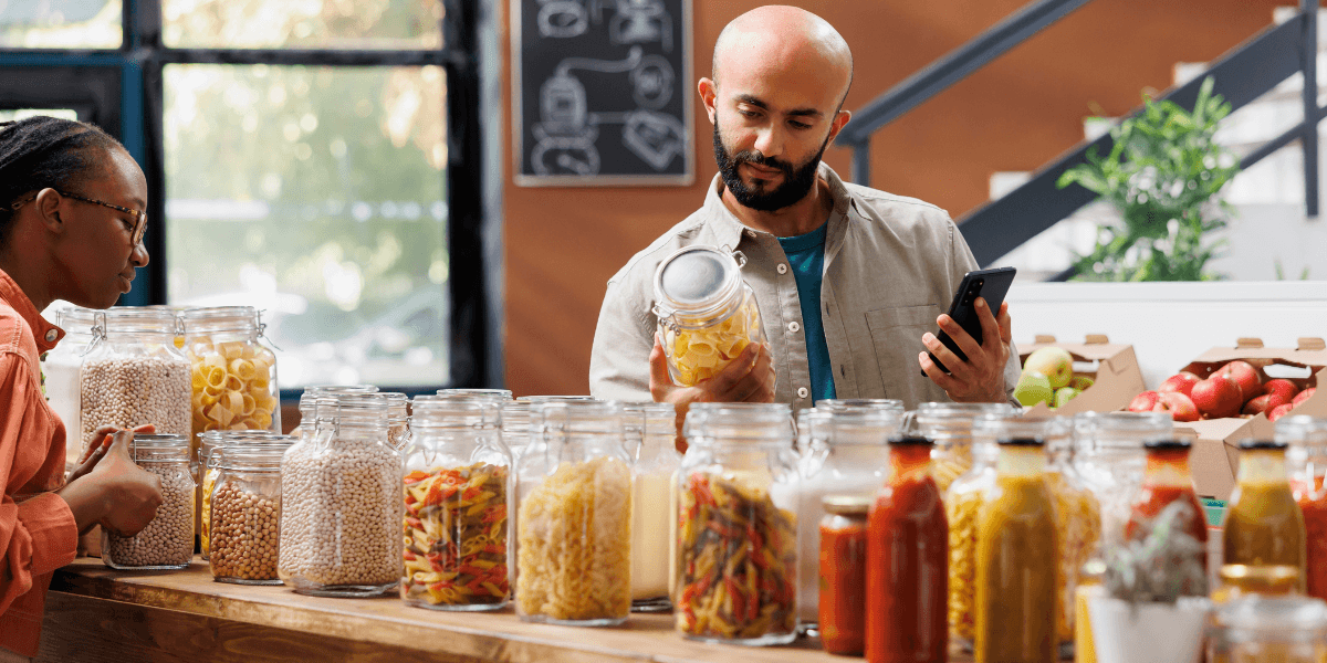 Two people examining various food jars placed on a kitchen counter, engaged in conversation about the items.